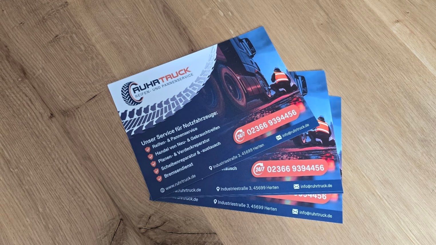 RuhrTruck-Flyer mit 24/7-Notrufnummer, Adresse und Leistungen auf einem Holztisch